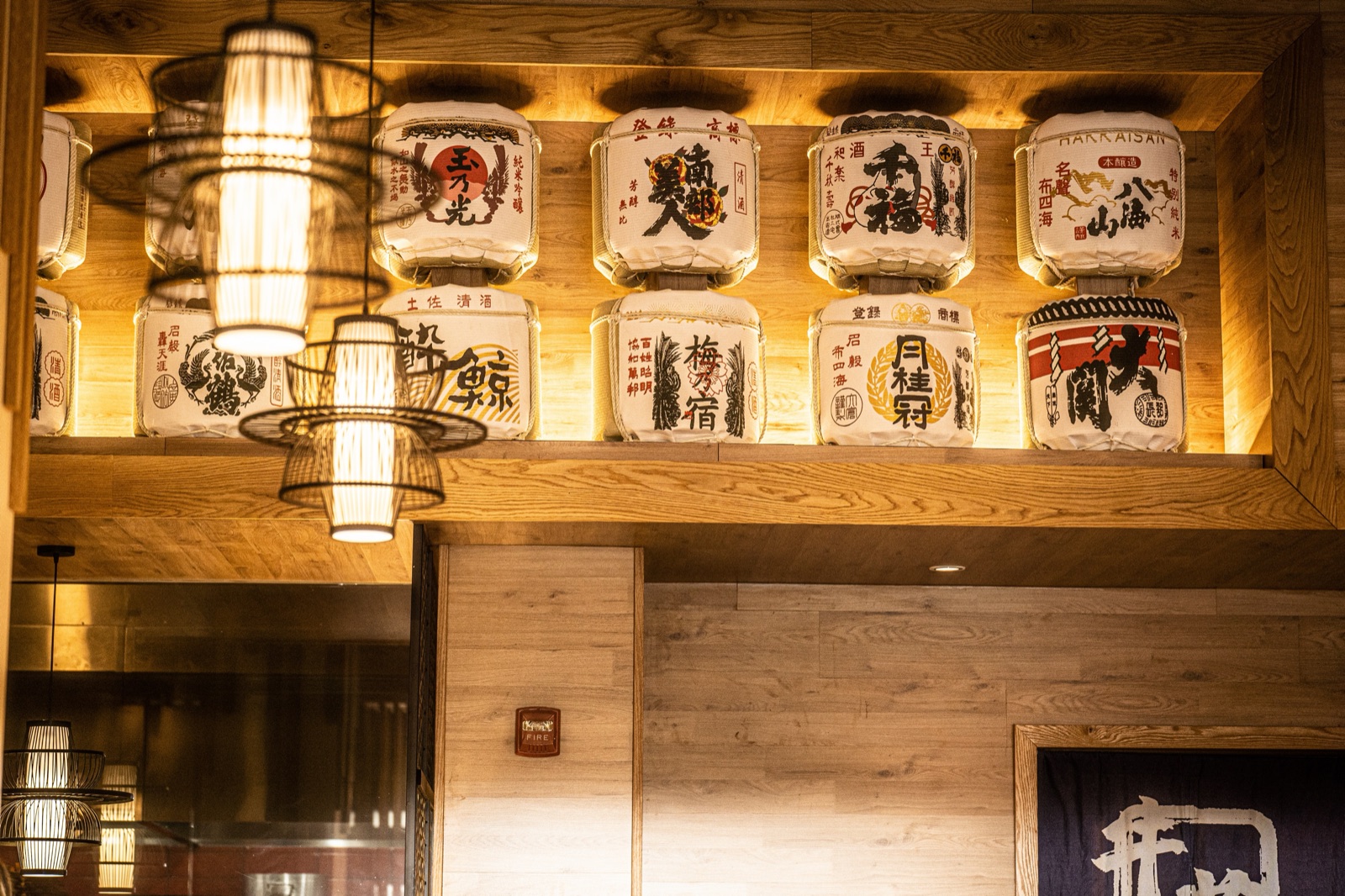 Barriles de sake en un estante de madera iluminado sobre el comedor de Gyuzo BBQ en Rockville