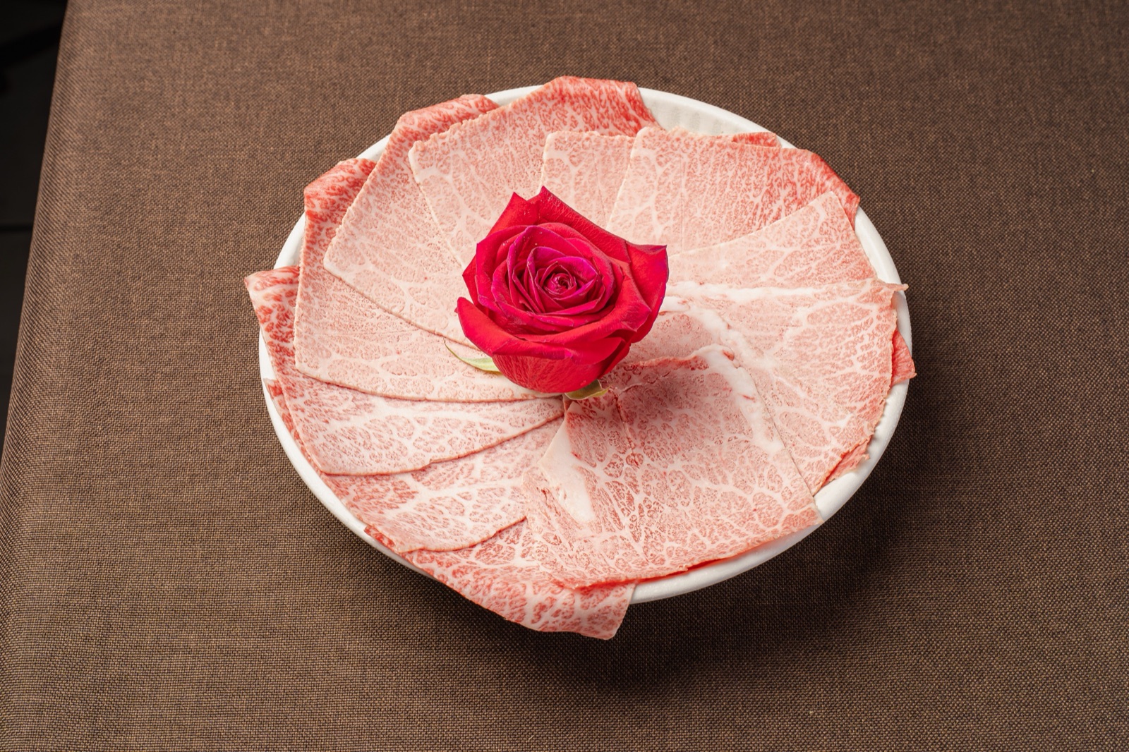 Finas lonchas de Wagyu A5 marmoleado alrededor de una rosa roja en Gyu Shige