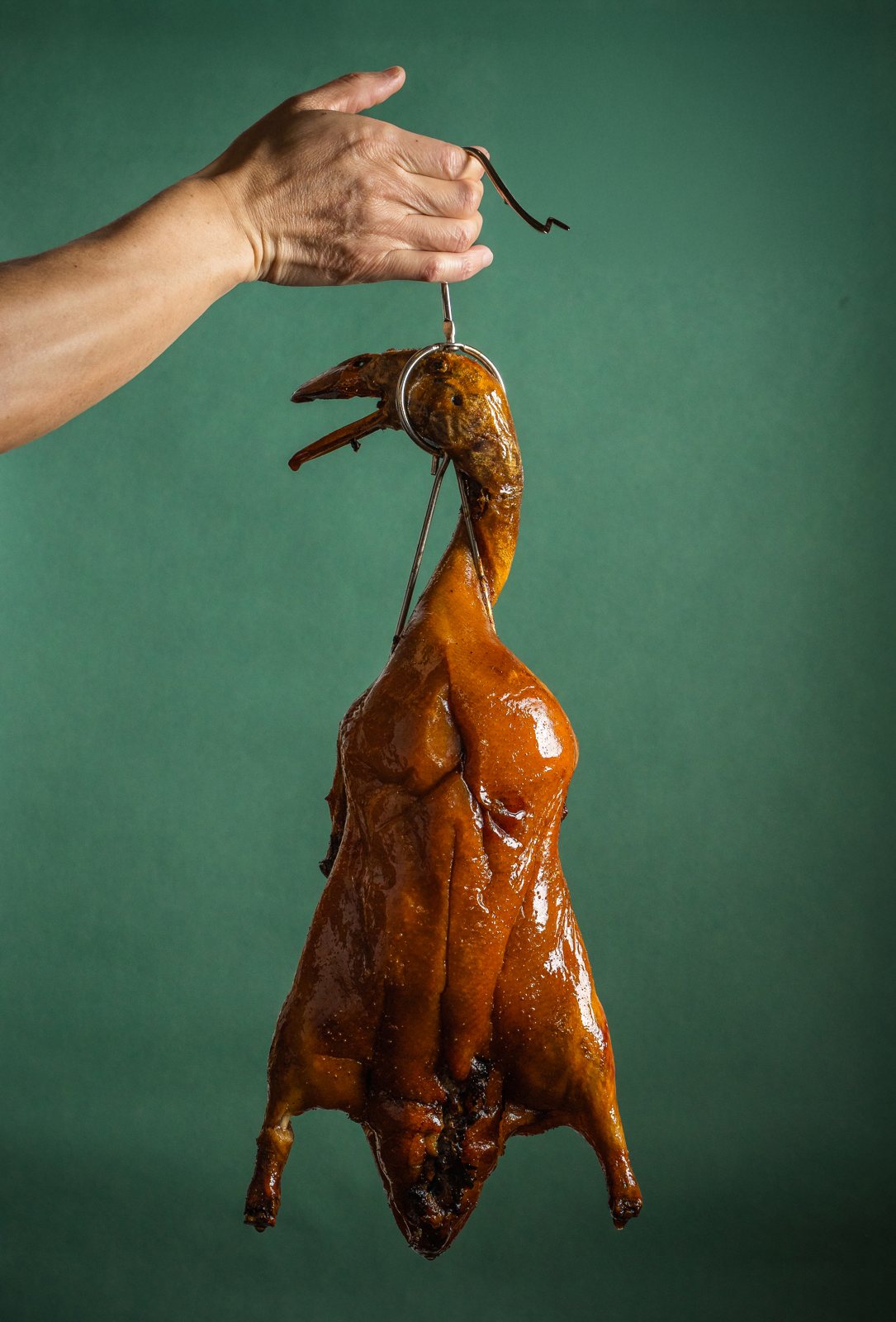 A whole Golden Peking Duck held up by its hook