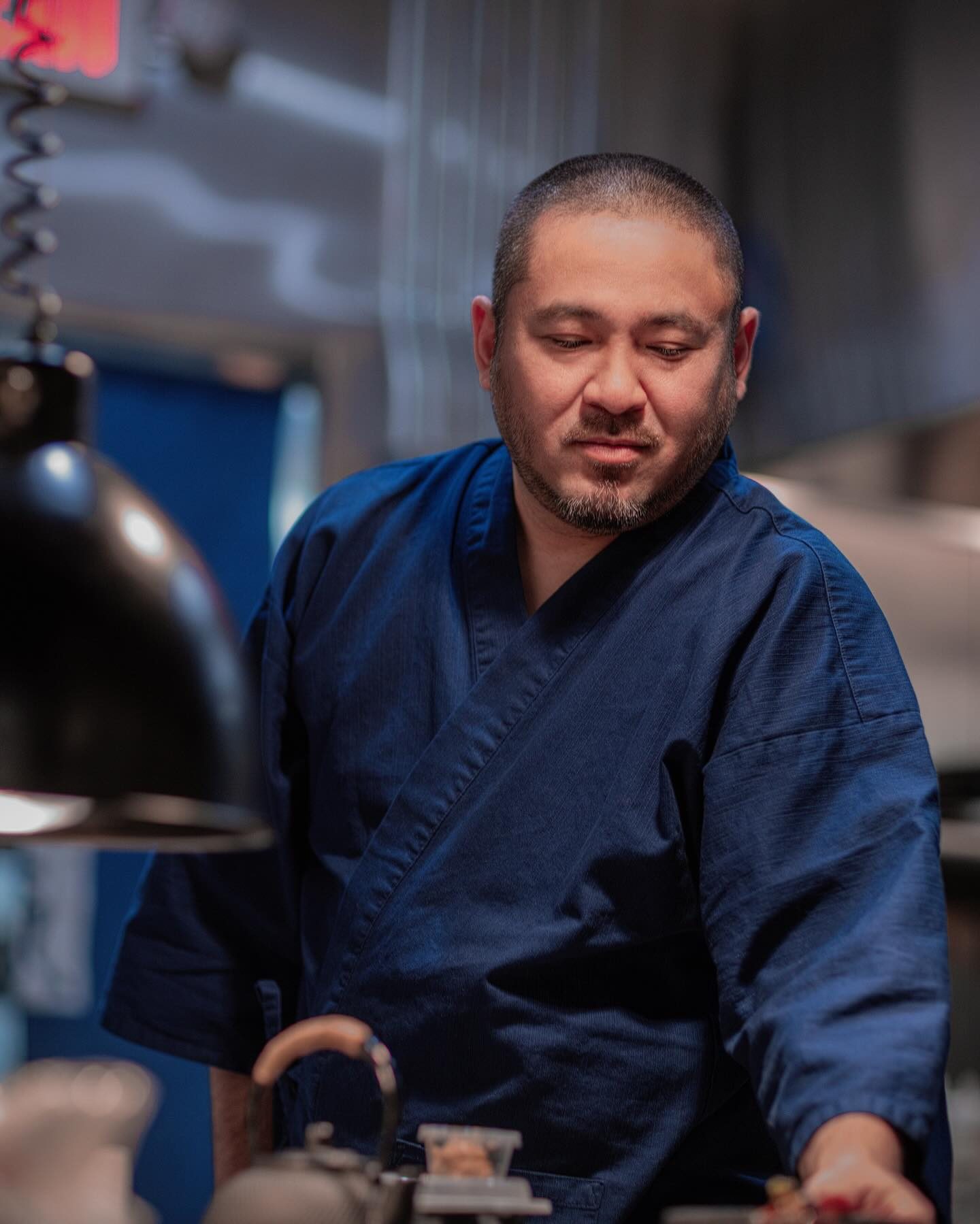 Chef Junzo Miyajima in a navy samue jacket standing at a kitchen station under a black hanging lamp