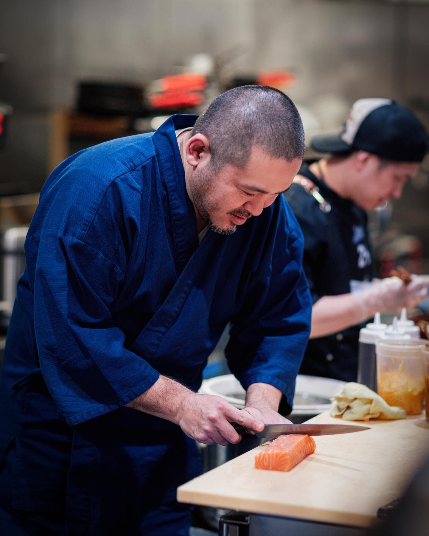 Chef Junzo Miyajima bending over a wood counter, slicing a block of salmon with a long knife