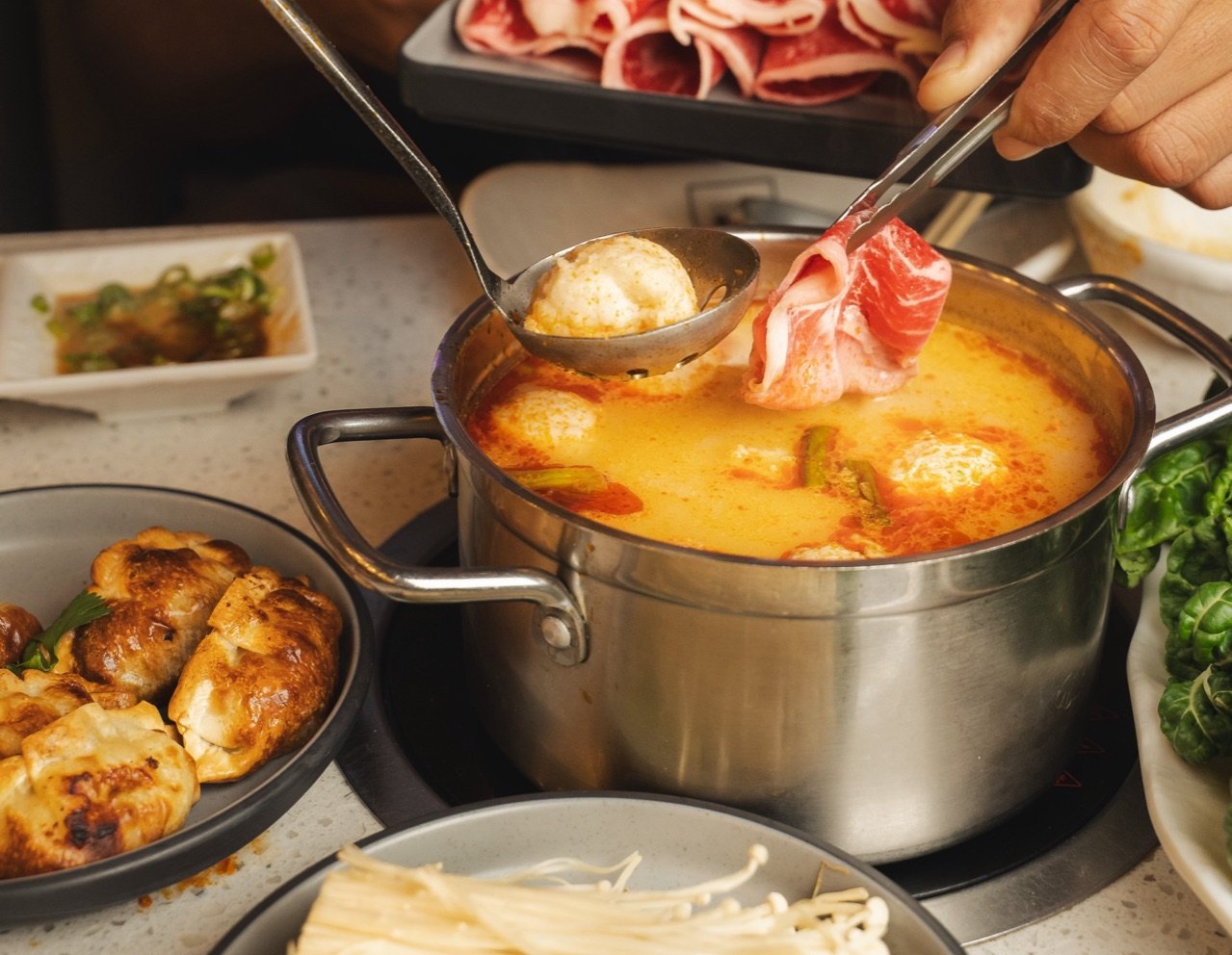 Urban Hot Pot 的一人一锅:橙色汤底里,汤勺舀起一颗丸子,一片雪花牛肉正在锅中涮煮