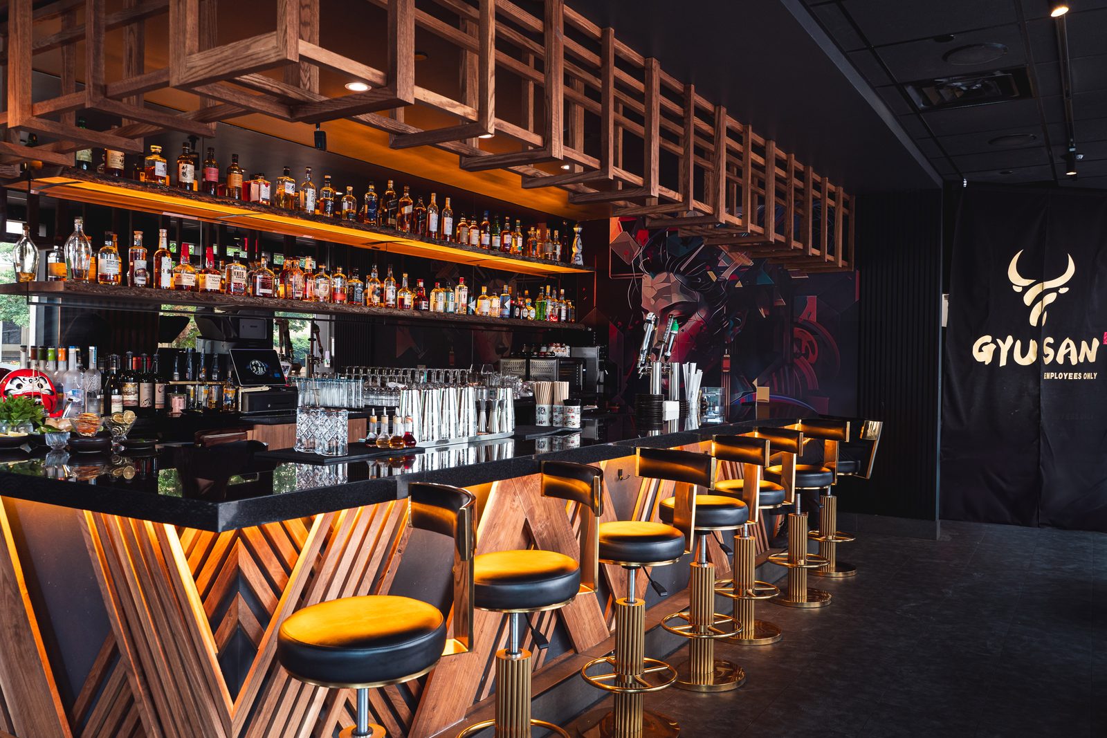 The backlit bar at Gyu San Arlington, with a gold-framed shelf wall and a large geisha mural