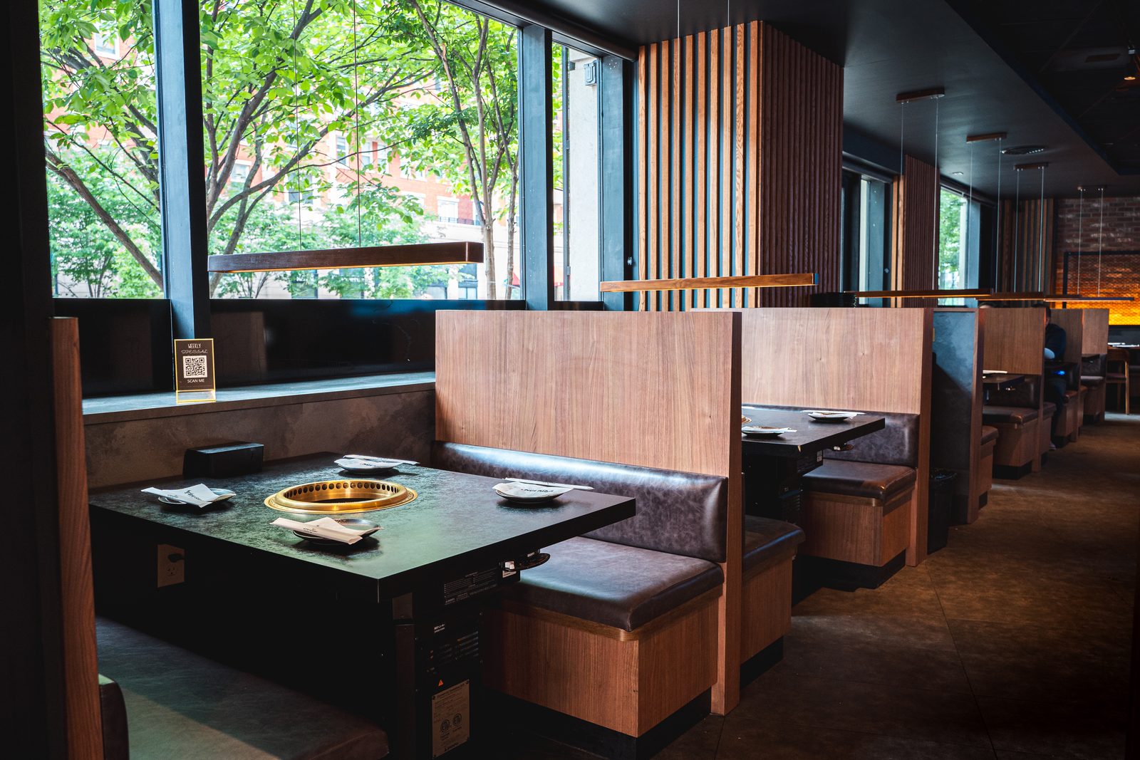 Wood-slat booths with built-in tabletop grills beside tall windows at Gyu San Arlington