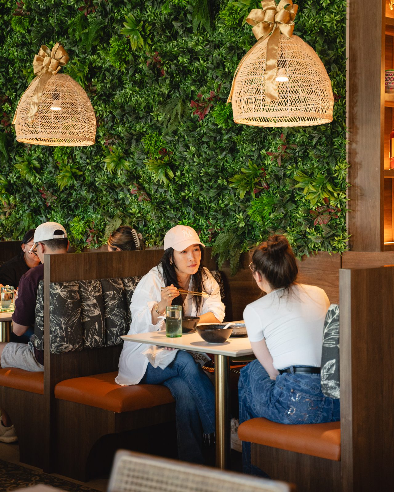 Guests at a booth under rattan lanterns and a living green wall at Southeast Impression