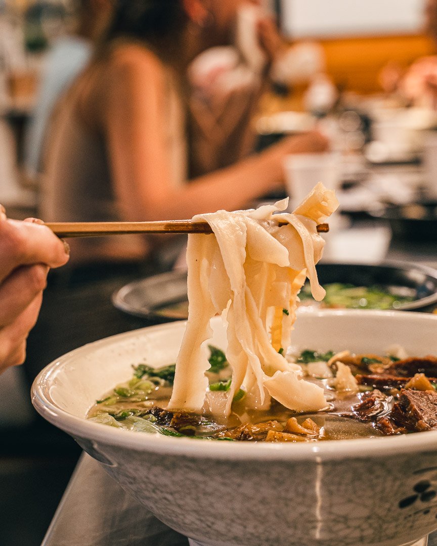 Wide hand-pulled noodles lifted from a bowl of beef noodle soup at Wasai in Washington, D.C.